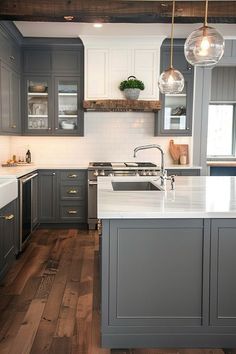 a kitchen with gray cabinets and white counter tops, wood floors and hanging lights over the sink