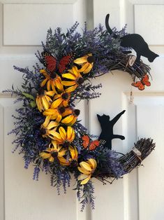 a wreath with yellow and purple flowers is hanging on the front door, next to a black cat figurine