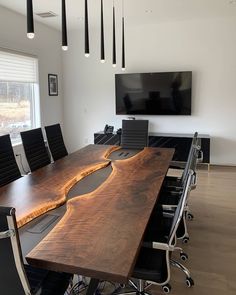 a large wooden table with black chairs in front of a flat screen tv mounted on the wall