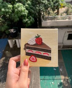 a hand holding up a piece of cake with strawberries on top and chocolate icing