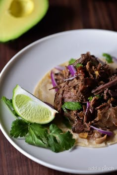 a white plate topped with meat, onions and cilantro next to an avocado