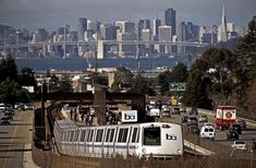 a white train traveling down tracks next to a city filled with tall buildings and traffic