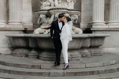 a man and woman standing next to each other in front of a fountain