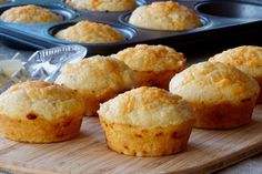 several muffins sitting on a wooden board next to a tray of other muffins