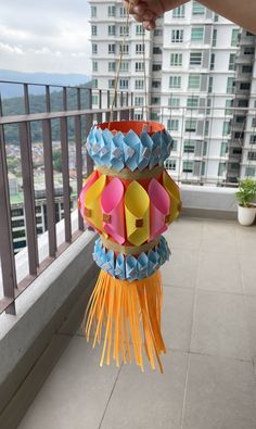 a person is holding up some paper decorations on a balcony with buildings in the background