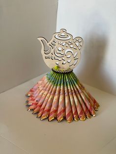 an intricately designed teapot made out of colored pencils on a white surface