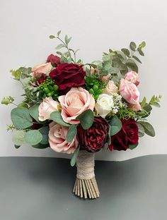 a bridal bouquet with roses and greenery on a gray table top, ready to be used as a centerpiece