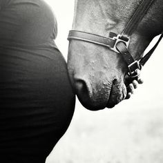 a black and white photo of a pregnant woman holding the reins of a brown horse