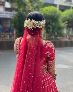 the back of a woman's head wearing a red lehenga with flowers in her hair