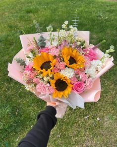 a person holding a bouquet of flowers in their hand on the grass near some trees