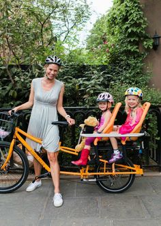 a woman and two small children on a bike with safety gear in front of them