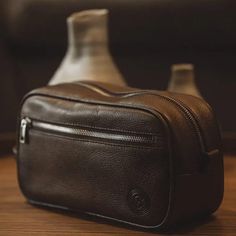 a brown leather bag sitting on top of a wooden table next to a glass bottle