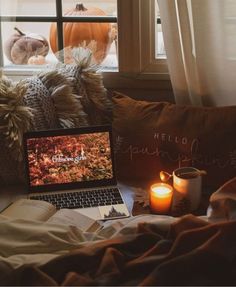 an open laptop computer sitting on top of a bed next to a candle and pillows