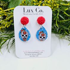 a pair of earrings with red beads and a skull on the front, sitting next to some flowers