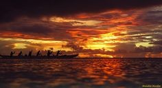 a group of people riding on the back of a boat under a cloudy sky at sunset