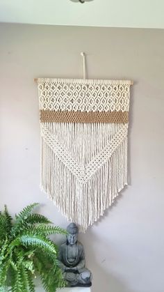 a white wall hanging on the side of a wall next to a potted plant