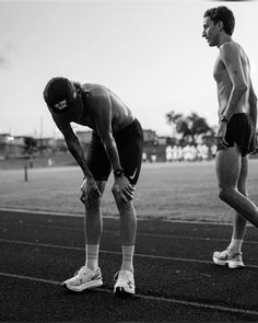 two men are standing on a track with their hands in their pockets as they look down at the ground