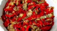 a white bowl filled with lots of red peppers and meat mixed in seasoning, sitting on a table