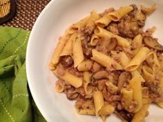 a white plate topped with pasta and meat covered in sauce on top of a table