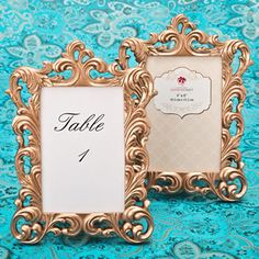 two ornate gold frames are sitting on a blue tablecloth with a place card holder in the middle