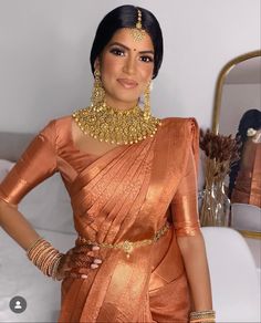 a woman in an orange sari with gold jewelry on her neck and hands on her hips