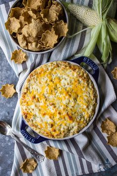 two bowls filled with dip and chips next to corn on the cob