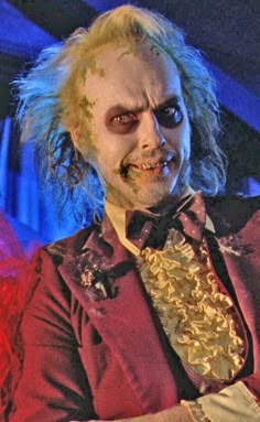 a man dressed up as the joker with makeup on his face and hair is holding something in his hand