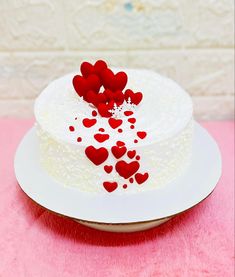 a white cake topped with red hearts on top of a pink tableclothed surface