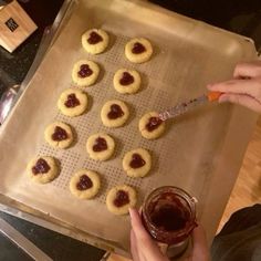 a person is holding a spoon over some cookies on a baking sheet with jam in the middle