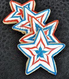 three decorated cookies with red, white and blue icing on a black tablecloth