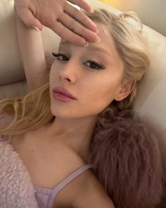 a woman laying on top of a couch next to a white pillow and holding her hand over her head