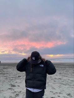 a woman standing on top of a sandy beach next to the ocean under a cloudy sky