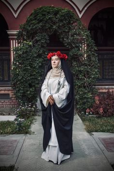 a woman dressed in black and white with red flowers on her head is standing outside