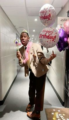 a man in a suit and tie holding balloons with the words happy birthday on them