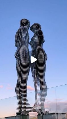 two metal statues are facing each other in front of a blue sky with white clouds