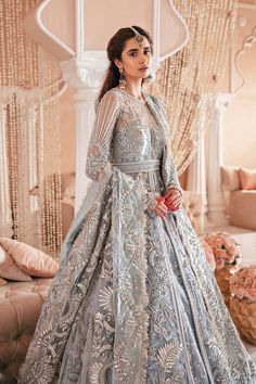 a woman in a blue and silver wedding gown standing on a couch with her hands behind her back