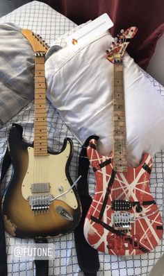 two guitars are laying next to each other on a bed