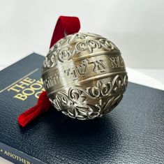 a silver bell on top of a book with a red ribbon around it's neck