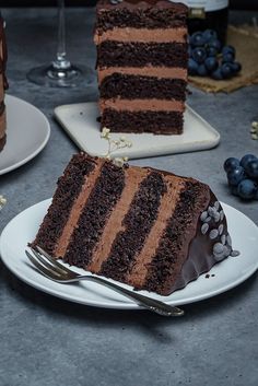 two slices of chocolate cake on white plates with blueberries and wine in the background