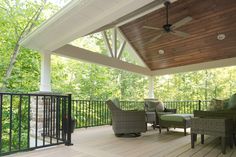 a covered deck with chairs and tables under a ceiling fan on top of the roof