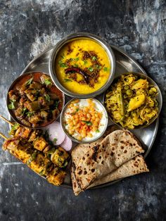 a metal plate topped with different types of food next to pita bread and vegetables