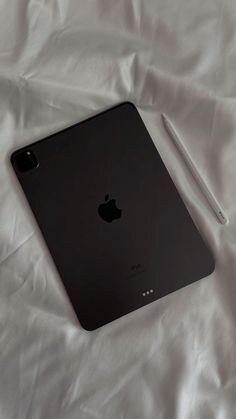 an ipad with a pen on top of it sitting on a white sheeted surface