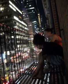 two people sitting on a bench in front of a cityscape at night time