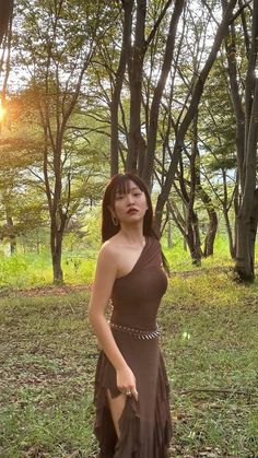 a woman in a brown dress posing for the camera with trees in the back ground