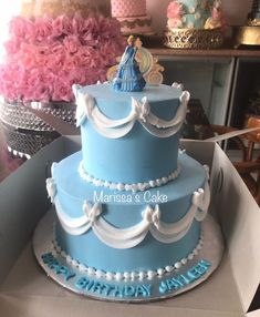 a three tiered blue cake with princess figurines on top in a box