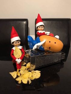 two elfs are sitting on the couch with potato chips in front of them and one is eating an orange