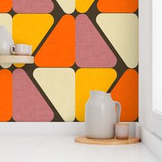 an orange, yellow and pink wallpaper with geometric shapes on the wall next to two white vases