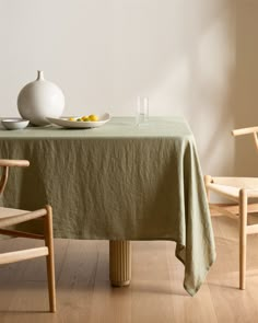 a white vase sitting on top of a table next to a bowl of fruit and two chairs