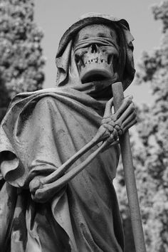 a black and white photo of a statue of a skeleton holding a stick with trees in the background