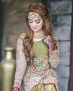 a woman with long hair wearing a green and gold outfit, standing in front of a vase